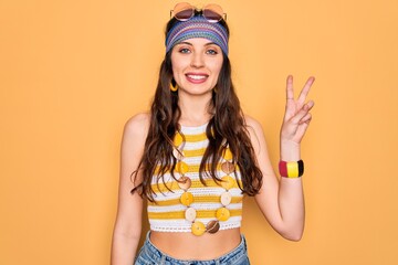 Young beautiful hippie woman with blue eyes wearing accesories and sunnglasses smiling looking to the camera showing fingers doing victory sign. Number two.