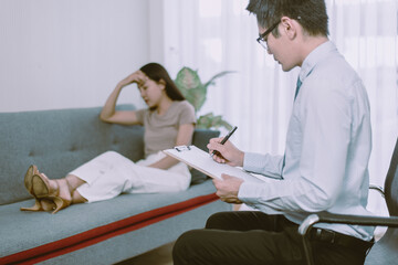 Professional psychologist talking with asian woman patient and writing notes,Therapist conducting a...