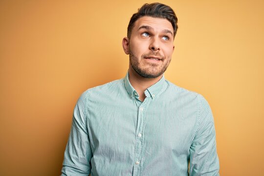 Young business man with blue eyes wearing elegant green shirt over yellow background smiling looking to the side and staring away thinking.