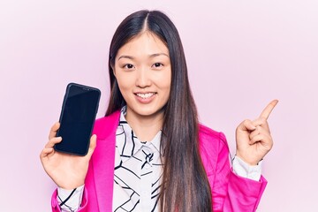 Young beautiful chinese woman holding smartphone showing screen smiling happy pointing with hand and finger to the side