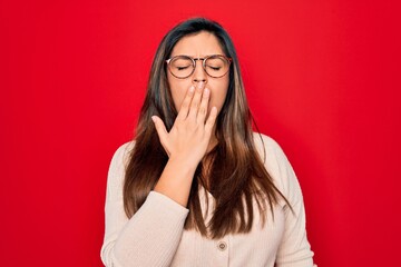 Young hispanic smart woman wearing glasses standing over red isolated background bored yawning tired covering mouth with hand. Restless and sleepiness.