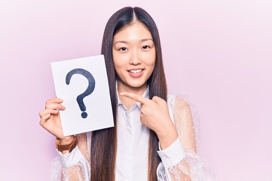 Young beautiful chinese woman holding question mark smiling happy pointing with hand and finger