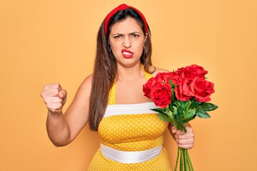 Young hispanic pin up woman wearing fashion sexy 50s style holding bouquet of red roses annoyed and frustrated shouting with anger, crazy and yelling with raised hand, anger concept