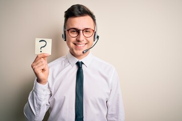 Young call center operator man wearing headset holding paper note with question mark with a happy face standing and smiling with a confident smile showing teeth