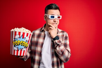 Young handsome caucasian man wearing 3d movie glasses and eating popcorn Thinking worried about a question, concerned and nervous with hand on chin