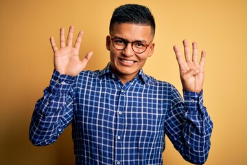 Naklejka premium Young handsome latin man wearing casual shirt and glasses over yellow background showing and pointing up with fingers number nine while smiling confident and happy.