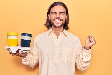 Young handsome man holding coffee to takeaway screaming proud, celebrating victory and success very excited with raised arm