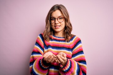 Young beautiful blonde girl wearing glasses and casual sweater over pink isolated background Smiling with hands palms together receiving or giving gesture. Hold and protection