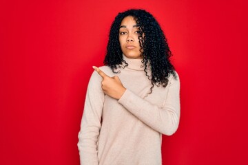 Young african american curly woman wearing casual turtleneck sweater over red background Pointing with hand finger to the side showing advertisement, serious and calm face