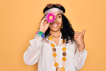 Young african american curly hippie woman wearing sunglasses holding pink flower on eye pointing...