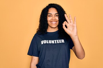 Young african american curly woman doing volunteering wearing volunteer t-shirt doing ok sign with...