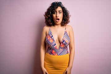 Young beautiful arab woman on vacation wearing swimsuit and sunglasses over pink background In shock face, looking skeptical and sarcastic, surprised with open mouth