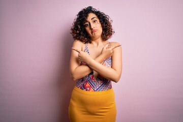 Young beautiful arab woman on vacation wearing swimsuit and sunglasses over pink background Pointing to both sides with fingers, different direction disagree