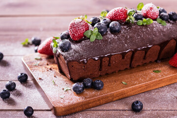 Fresh tasty homemade chocolate cake with icing with summer berries on a wooden table.