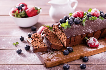 Fresh tasty homemade chocolate cake with icing with summer berries on a wooden table.