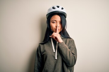 Young beautiful chinese woman wearing bike helmet over isolated white background asking to be quiet with finger on lips. Silence and secret concept.