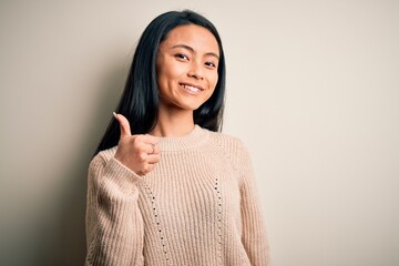 Young beautiful chinese woman wearing casual sweater over isolated white background doing happy thumbs up gesture with hand. Approving expression looking at the camera showing success.