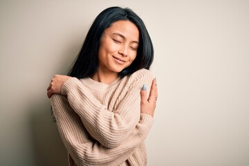 Young beautiful chinese woman wearing casual sweater over isolated white background Hugging oneself...