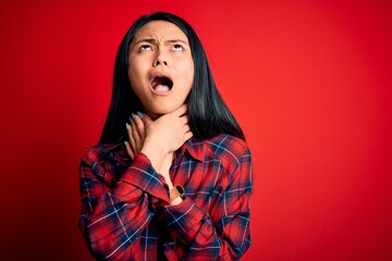 Young beautiful chinese woman wearing casual shirt over isolated red background shouting suffocate because painful strangle. Health problem. Asphyxiate and suicide concept.