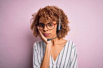 African american curly call center agent woman working using headset over pink background thinking looking tired and bored with depression problems with crossed arms.