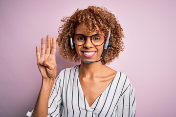 African american curly call center agent woman working using headset over pink background showing and pointing up with fingers number four while smiling confident and happy.