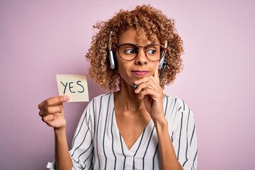 African american call center agent woman using headset holding reminder with yes message serious...