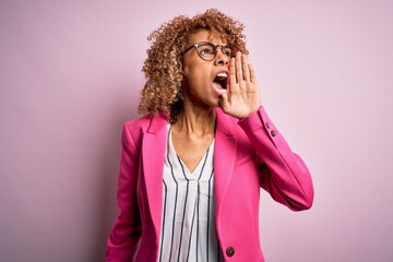 Fototapeta na wymiar Young african american businesswoman wearing glasses standing over pink background shouting and screaming loud to side with hand on mouth. Communication concept.