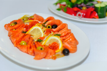 Slicing salmon on a plate close-up selective focus. Cold appetizer of red fish decorated with red caviar, lemon, herbs and olives.