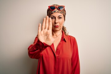Middle age brunette woman wearing handkerchief on head and shirt over white background doing stop sing with palm of the hand. Warning expression with negative and serious gesture on the face.