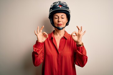 Middle age motorcyclist woman wearing motorcycle helmet over isolated white background relax and smiling with eyes closed doing meditation gesture with fingers. Yoga concept.