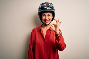 Middle age motorcyclist woman wearing motorcycle helmet over isolated white background smiling positive doing ok sign with hand and fingers. Successful expression.