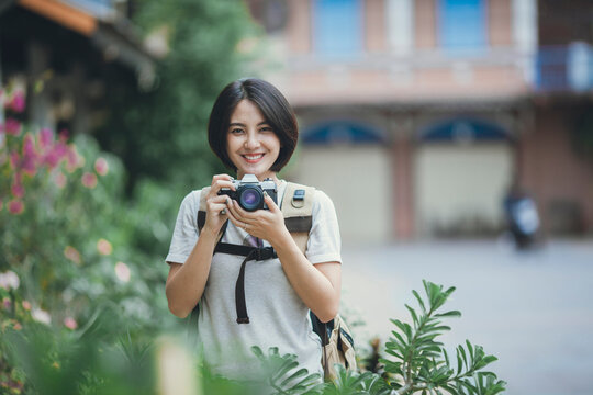 Beautiful Asian woman short hair style backpacker holding camera travel on street. Young girl backpack smiling with camera.