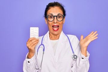 Middle age senior professional doctor woman holding pharmaceutical pills very happy and excited, winner expression celebrating victory screaming with big smile and raised hands