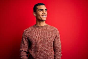 Obraz premium Young handsome african american man wearing casual sweater standing over red background looking away to side with smile on face, natural expression. Laughing confident.