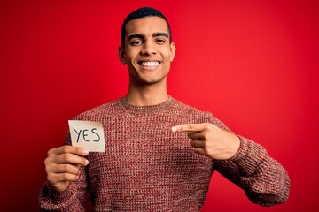 Young handsome african american man holding reminder paper with yes message very happy pointing...