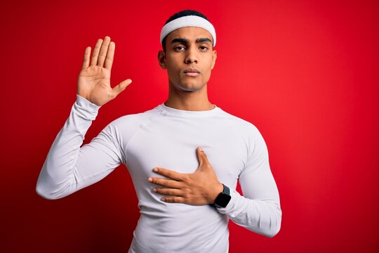 Young handsome african american sportsman wearing sportswear over red background Swearing with hand on chest and open palm, making a loyalty promise oath