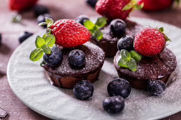 Chocolate cakes (cupcakes) are on the table. Cupcakes decorated  blueberries, strawberries and green leaves mint on top. Beautiful and elegant serving with white dishes