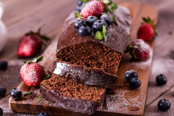 Fresh tasty homemade chocolate cake with icing with summer berries on a wooden table.