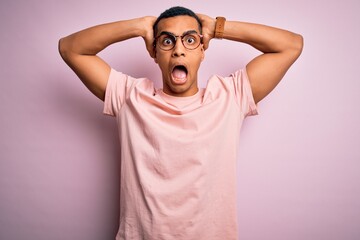 Fototapeta na wymiar Handsome african american man wearing casual t-shirt and glasses over pink background Crazy and scared with hands on head, afraid and surprised of shock with open mouth