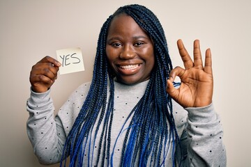 Young african american plus size woman with braids holding reminder paper with yes message doing ok...