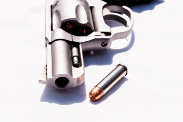 A stainless snub nosed 357 magnum revolver with a hollow point bullet next to it on a white...