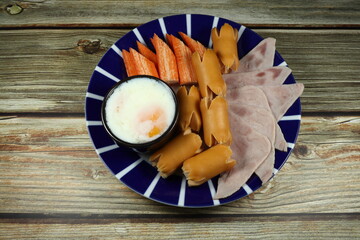 Famous traditional fusion breakfast in Asia, boiled soft chicken egg, cutting pork ham, smoked pork sausage and chopped crab stick on the plate. High nutrition and power in the morning. 