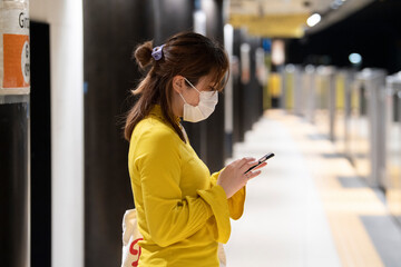 地下鉄のホームで電車を待つマスク姿の女性