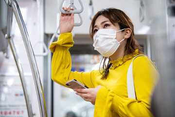 電車でつり革を掴むマスクをした女性