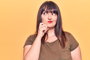 Young plus size woman wearing casual clothes thinking concentrated about doubt with finger on chin and looking up wondering