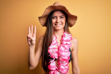 Young beautiful woman with blue eyes on vacation wearing bikini and hawaiian lei showing and pointing up with fingers number three while smiling confident and happy.