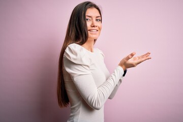 Young beautiful woman with blue eyes wearing casual white t-shirt over pink background pointing aside with hands open palms showing copy space, presenting advertisement smiling excited happy