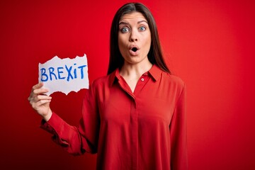 Young beautiful woman with blue eyes holding paper with brexit message over red background scared in shock with a surprise face, afraid and excited with fear expression
