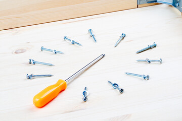 an orange screwdriver and wood screws are located around it