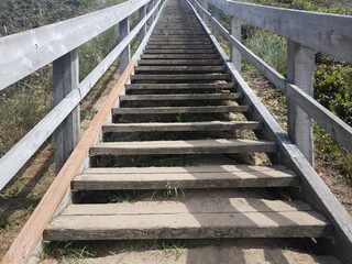 wooden stairs going up hill with railing and sand